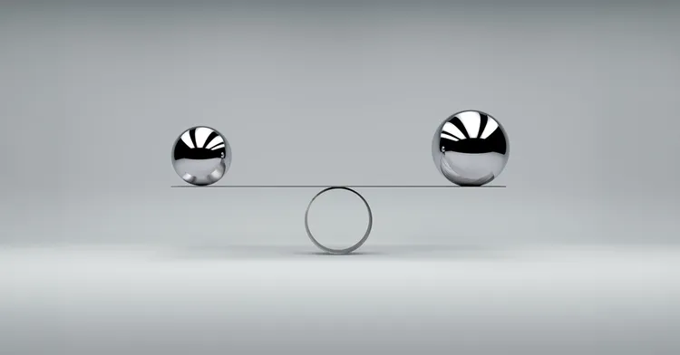 Zwei Metallkugeln im Gleichgewicht auf einer Wippe als Symbol für Stabilisierung, Tragfähigkeit und finanzielle Balance